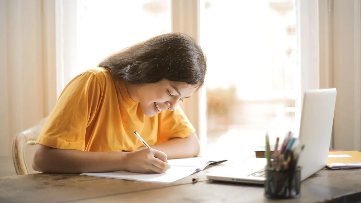 žena u okna píše poznámky vedle otevřeného notebooku