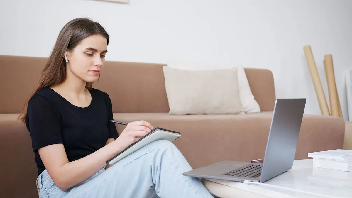 žena sedí na gauči s poznámkovým blokem a notebookem