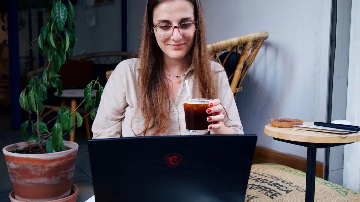 Žena v brýlích pije kávu při práci na notebooku
