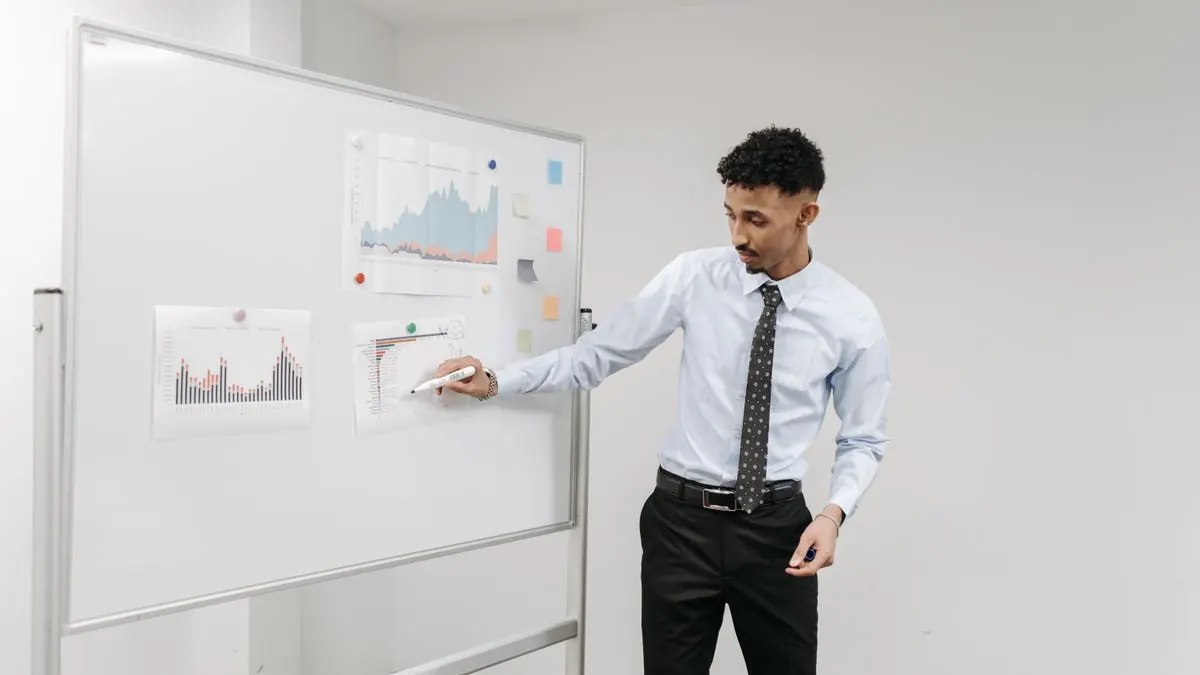 Muž v košili ukazuje na grafy připevněné na bílé tabuli