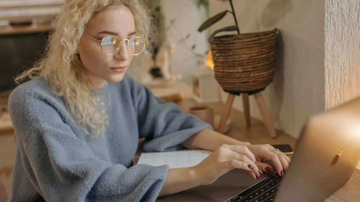 Žena s kudrnatými vlasy soustředěně pracuje na notebooku doma