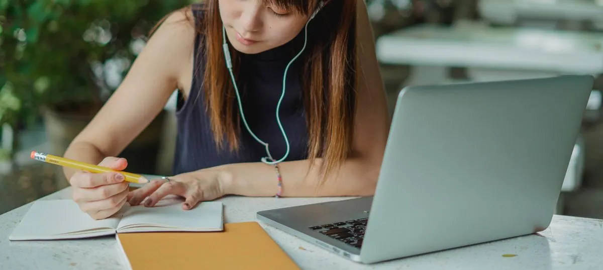 dívka se sluchátky se učí s notebookem a sešitem