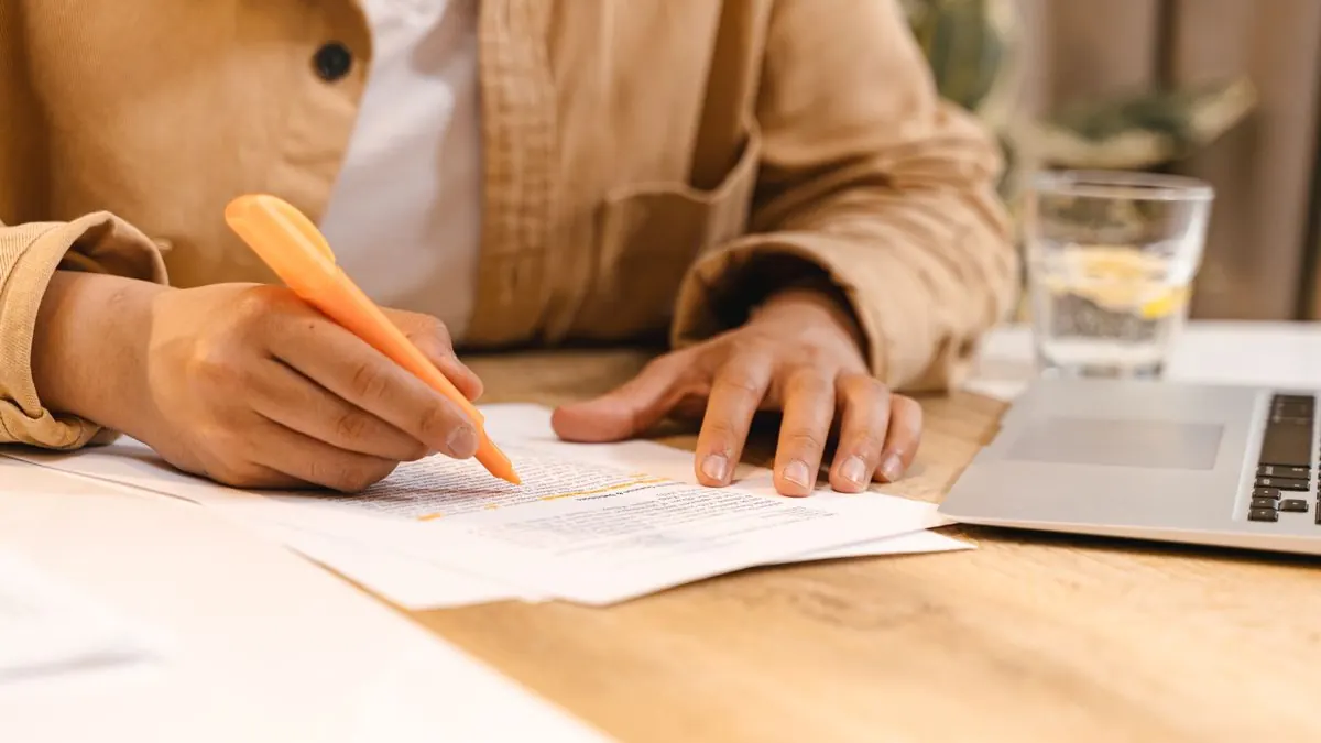 člověk píše poznámky na papír vedle otevřeného notebooku