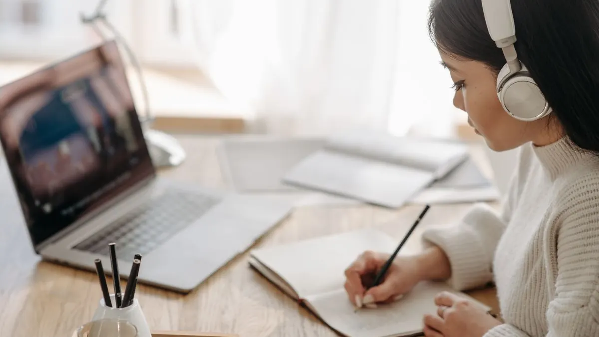 Žena se sluchátky dělá si poznámky během online studia