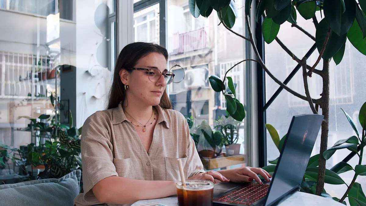 Žena pracuje na notebooku u okna mezi rostlinami