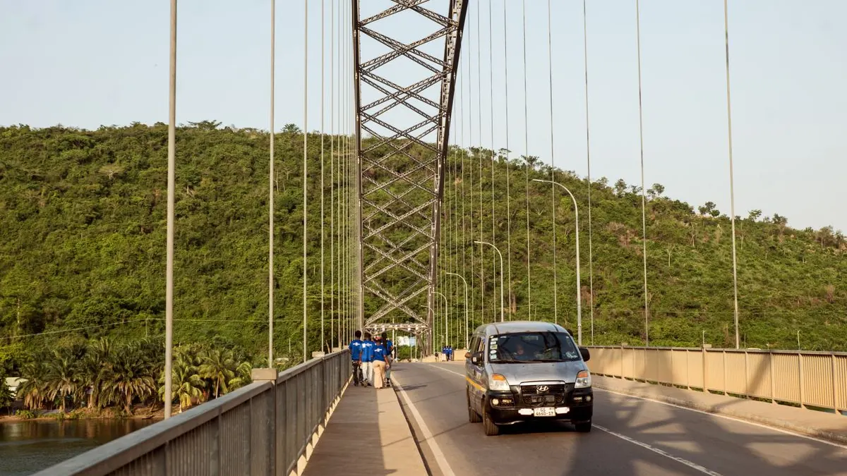 Auto projíždí po visutém mostě mezi zelenými kopci