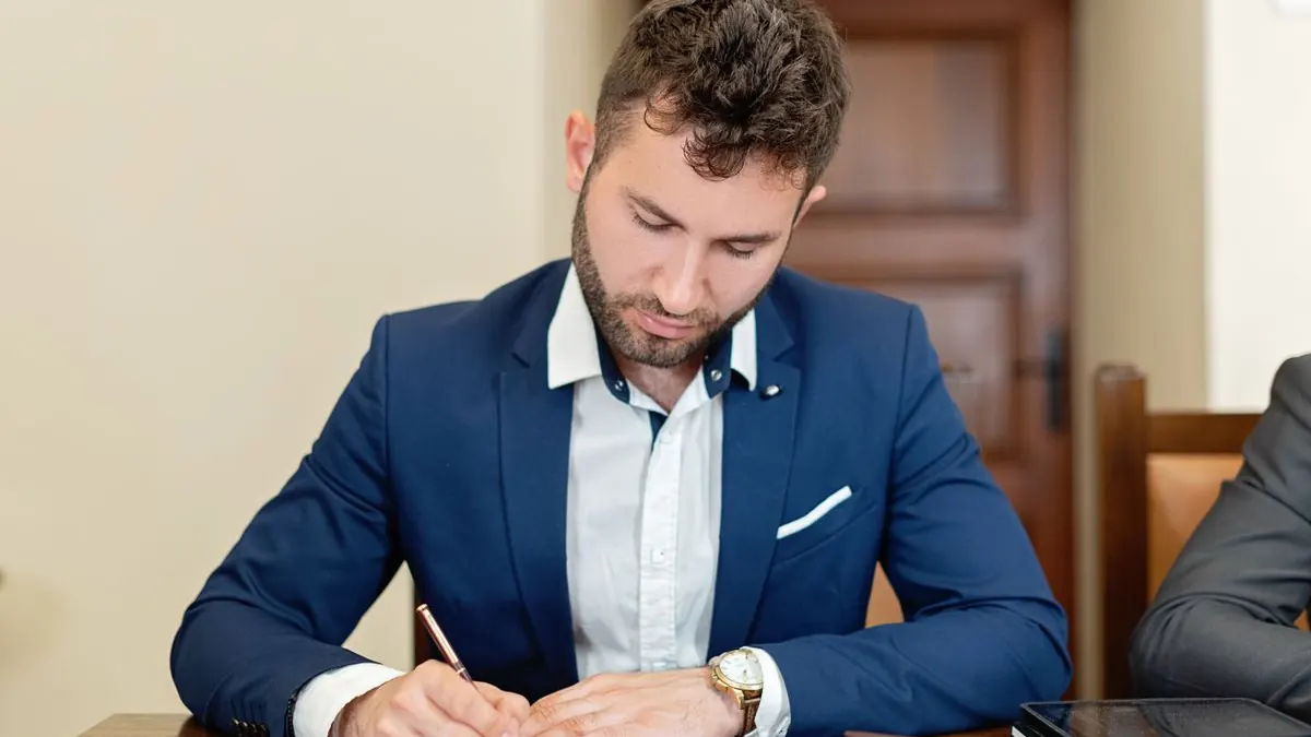 Muž v obleku podepisuje smlouvu u stolu