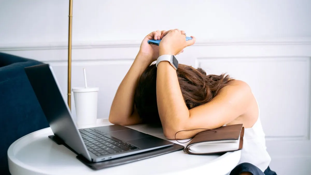 Žena položila hlavu na stůl vedle otevřeného notebooku