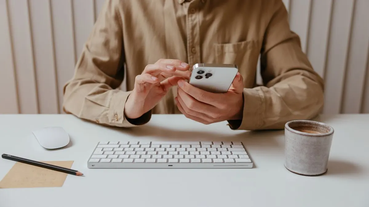Muž u stolu píše na telefonu vedle klávesnice a kávy