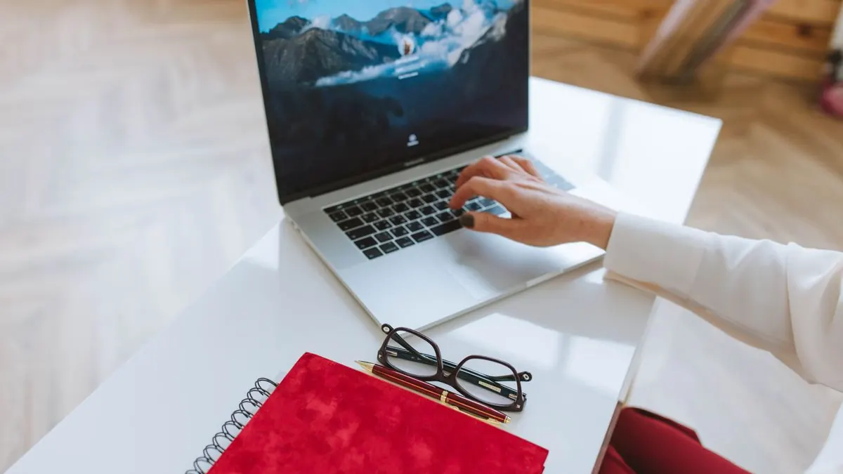 Otevřený notebook s horskou tapetou vedle sešitů a brýlí